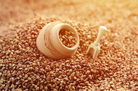 Background image of a large pile of buckwheat, in the middle of which lies a small jug and a wooden spatula for cerealsの写真素材