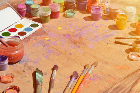 Still life, showing an interest in watercolor painting and art. A lot of brushes, jars with watercolor paint and used gouache lie on an old wooden surface, which is smeared into colorful spotsの写真素材