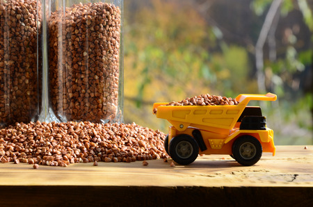 A small yellow toy truck is loaded with brown grains of buckwheat around the buckwheat pile and a...