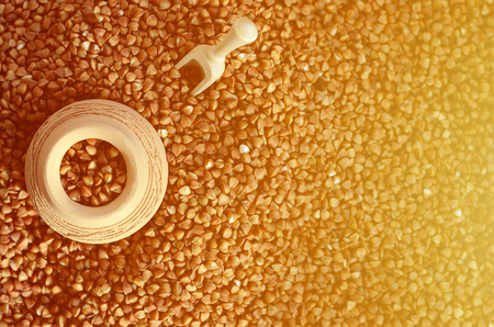 Background image of a large pile of buckwheat, in the middle of which lies a small jug and a wooden spatula for cerealsの写真素材