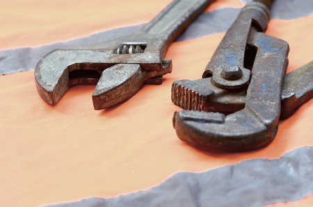 Adjustable and pipe wrenches against the background of an orange signal worker shirt. Still life associated with repair, railway or plumbing worksの写真素材