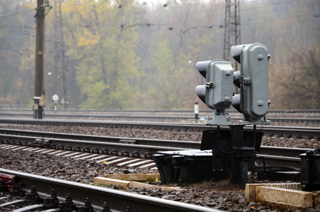 Photo of a fragment of a railway track with a small traffic light in rainy weatherの写真素材