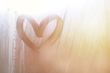 A heart-shaped drawing drawn by a finger on a misted glass in rainy weatherの写真素材