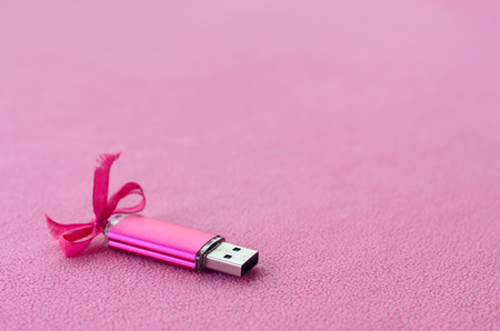 Brilliant pink usb flash memory card with a pink bow lies on a blanket of soft and furry light pink fleece fabric. Classic female gift design for a memory cardの写真素材