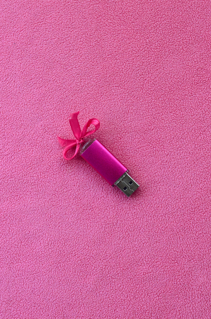 Brilliant pink usb flash memory card with a pink bow lies on a blanket of soft and furry light pink fleece fabric. Classic female gift design for a memory cardの写真素材