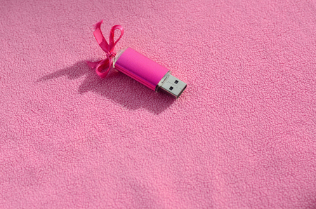 Brilliant pink usb flash memory card with a pink bow lies on a blanket of soft and furry light pink fleece fabric. Classic female gift design for a memory cardの写真素材