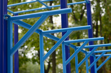 Blue metal pipes and cross-bars against a street sports field for training in athletics. Outdoor athletic gym equipment. Macro photo with selective focus and extremely blurred backgroundの写真素材