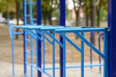 Blue metal pipes and cross-bars against a street sports field for training in athletics. Outdoor athletic gym equipment. Macro photo with selective focus and extremely blurred backgroundの写真素材