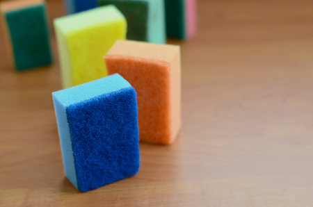A few kitchen sponges lie on a wooden kitchen countertop. Colorful objects for washing dishes and cleaning in the house are ready for useの写真素材