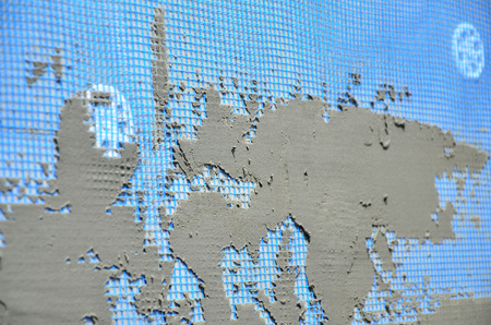The texture of the wall, covered with gray foam polystyrene plates, covered with a blue reinforcing mesh and covered with a mixture for gluing it. Stage of wall insulationの写真素材