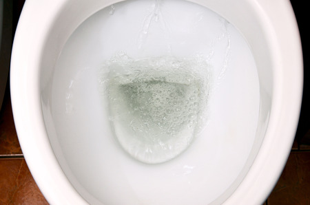A photo of a white ceramic toilet bowl in the process of washing it off. Ceramic sanitary ware for correcting the need with an automatic flushing deviceの写真素材