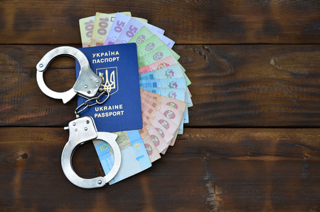 A photograph of a Ukrainian foreign passport, a certain amount of Ukrainian money and police handcuffs. Concept of illegal earnings of Ukrainian citizens abroadの写真素材