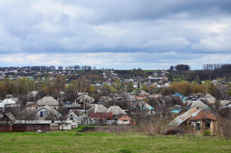 A rural landscape with many private houses and green trees. Suburban panorama on a cloudy afternoon. A place far from the cityの写真素材