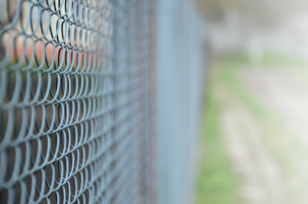 A photograph of a metal net used as a fence of private possessions. Old metal grid in perspective with a blurred backgroundの写真素材