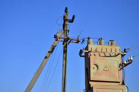 Old and obsolete electrical transformer against the background of a cloudless blue sky. Device for...