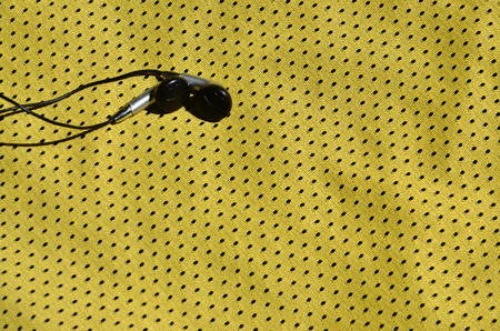 Black earphones lie on the yellow sportswear of polyester nylon fiber. The concept of listening to music during sports training with modern technologyの写真素材