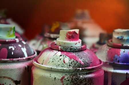 Still life with a large number of used colorful spray cans of aerosol paint lying on the treated wooden surface in the artist's graffiti workshop. Dirty and stained cans for spray artの写真素材