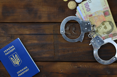 A photograph of a Ukrainian foreign passport, a certain amount of Ukrainian money and police handcuffs. Concept of illegal earnings of Ukrainian citizens abroadの写真素材