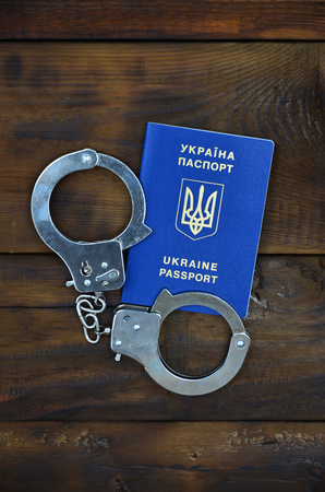 A Ukrainian passport with police handcuffs lies on a wooden table. Problems with the law during the crossing of the borders of countries. The illegal side of visa-free travel for Ukrainian citizensの写真素材