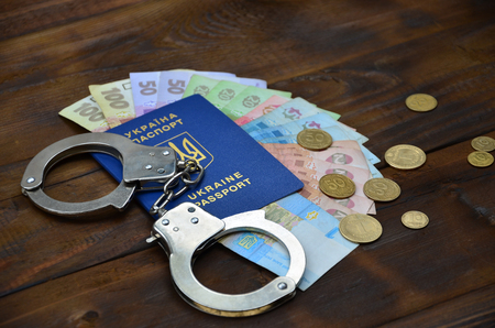 A photograph of a Ukrainian foreign passport, a certain amount of Ukrainian money and police handcuffs. Concept of illegal earnings of Ukrainian citizens abroadの写真素材