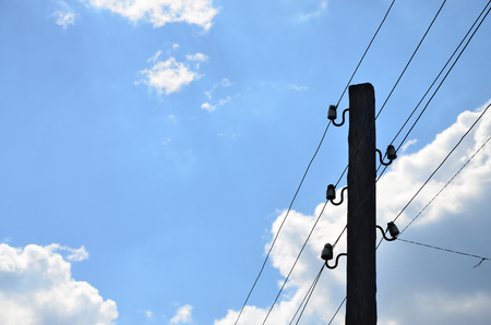 Old wooden electric pole for transmission of wired electricity on a background of a cloudy blue sky. Obsolete method of supplying electricity for later useの写真素材