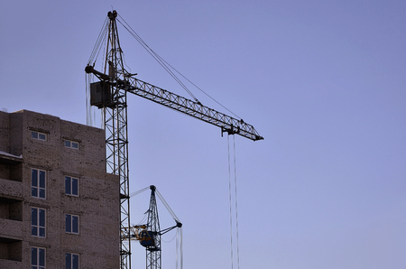 Working tall cranes inside place for with tall buildings under construction against a clear blue sky. Crane and building working progress with copyspaceの写真素材