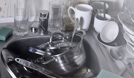 A huge pile of unwashed dishes in the kitchen sink and on the countertop. A lot of utensils and kitchen appliances before washing. The concept of daily cooking routine and complexityの写真素材