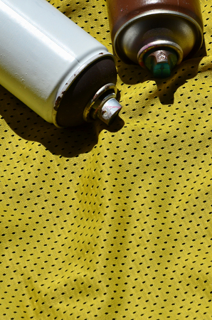 Several used aerosol paint sprayers lie on the sports shirt of a basketball player made of polyester fabric. The concept of youth street art, active sports and eventful lifestyleの写真素材