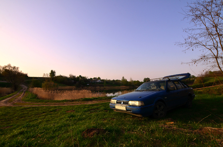 A blue car on a background of a rustic landscape with a wild cane field and a small lake. The family came to rest on the nature near the lakeの写真素材