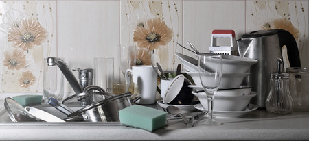 A huge pile of unwashed dishes in the kitchen sink and on the countertop. A lot of utensils and kitchen appliances before washing. The concept of daily cooking routine and complexityの写真素材