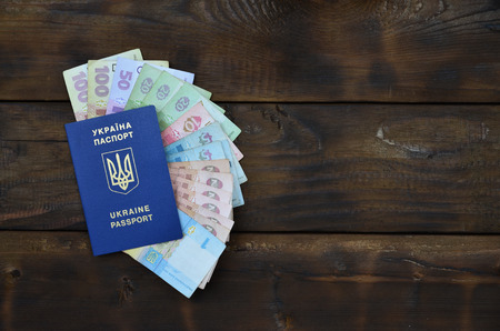 A photograph of a Ukrainian passport and a certain amount of Ukrainian money on a wooden surface....