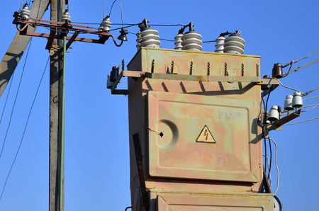 Old and obsolete electrical transformer against the background of a cloudless blue sky. Device for distribution of supply of high-voltage energyの写真素材
