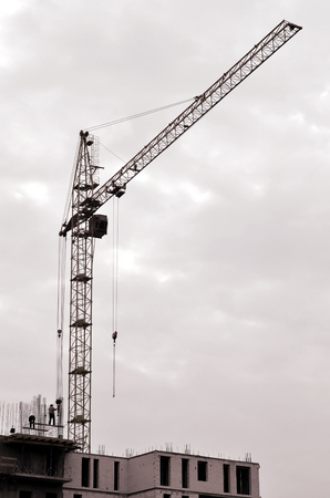 Working tall cranes inside place for with tall buildings under construction against a clear blue sky. Crane and building working progress. Retro toneの写真素材