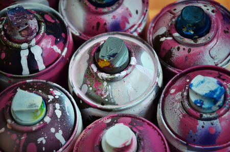 Still life with a large number of used colorful spray cans of aerosol paint lying on the treated wooden surface in the artist's graffiti workshop. Dirty and stained cans for spray artの写真素材