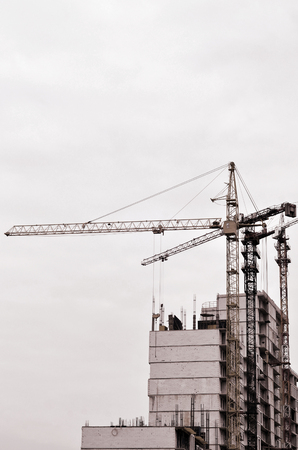 Working tall cranes inside place for with tall buildings under construction against a clear blue sky. Crane and building working progress. Retro toneの写真素材