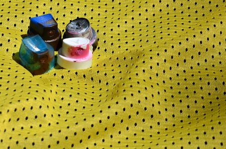Several caps for used aerosol paint sprayers lie on the sports shirt of a basketball player made of polyester fabric. The concept of youth street art, active sports and eventful lifestyleの写真素材