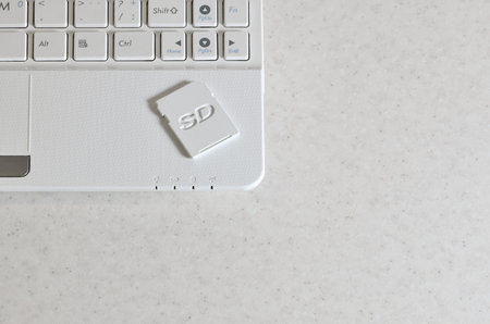 A compact SD memory card lies on a white netbook. The digital information storage device is ready...