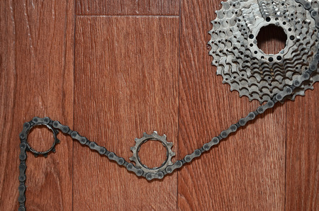 Some composition of a bicycle chain, several sprockets and other components of a sports bike. Metal and dirty bicycle parts on a brown wooden backgroundの写真素材