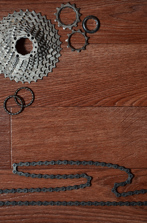 Some composition of a bicycle chain, several sprockets and other components of a sports bike. Metal and dirty bicycle parts on a brown wooden backgroundの写真素材