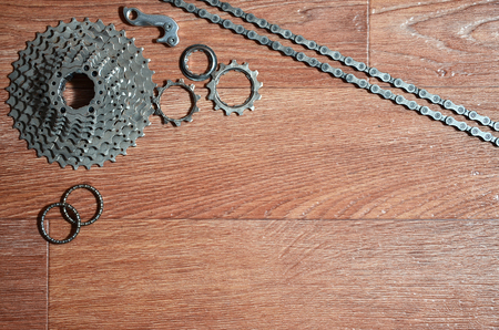 Some composition of a bicycle chain, several sprockets and other components of a sports bike. Metal and dirty bicycle parts on a brown wooden backgroundの写真素材