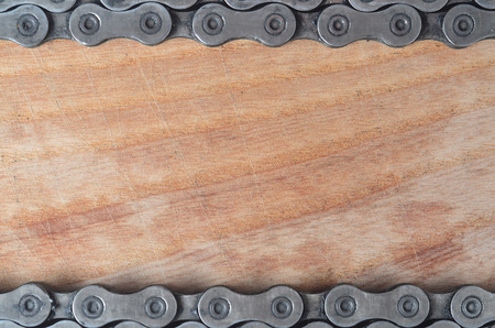 Background image of a chain from a mountain bike lying on a wooden table in a bicycle shop. One of...