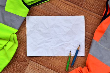 A crumpled sheet of paper with two pencils surrounded by green and orange working uniforms. Still life associated with repair, railway or plumbing worksの写真素材