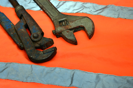 Adjustable and pipe wrenches against the background of an orange signal worker shirt. Still life associated with repair, railway or plumbing worksの写真素材