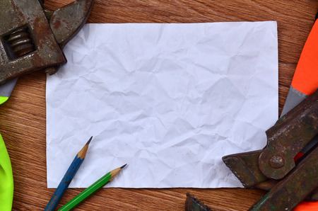 A crumpled sheet of paper with two pencils surrounded by green and orange working uniforms and adjustable wrenches. Still life associated with repair, railway or plumbing worksの写真素材
