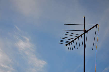An old and rusty television antenna against a cloudy blue sky. Obsolete device for receiving a television signal in private housesの写真素材