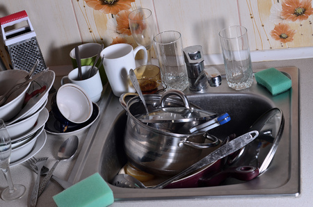 A huge pile of unwashed dishes in the kitchen sink and on the countertop. A lot of utensils and kitchen appliances before washing. The concept of daily cooking routine and complexityの写真素材