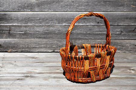 An empty wicker basket of wooden rods lies on a wooden surface against the background of a wall of black horizontal wooden boards. Patterned brown hand-made basketの写真素材