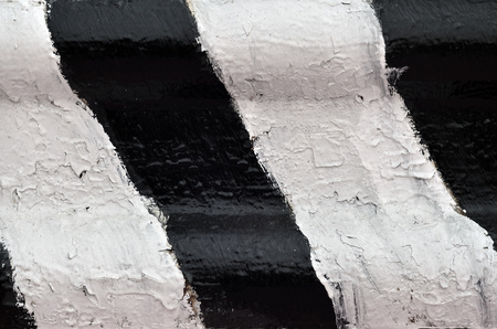 Close-up view of a metal barrier with striped color. An image of a hazard warning barrier that has been painted by hand in black and white colorsの写真素材