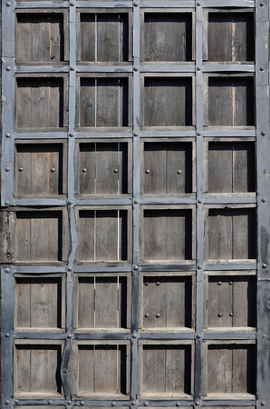 The texture of an antique wooden door from the 16th and 17th century. Ancient gates made of wooden boards, reinforced with metal forged fragmentsの写真素材