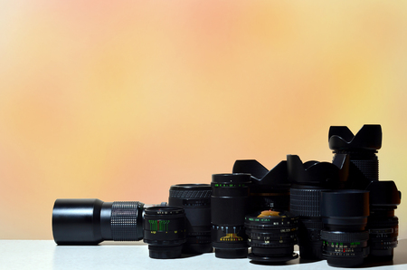 Many different lenses for SLR cameras lie on a colorless desk. Background image for a business card of a photographer or a photo equipment vendor. Equipment for professional photographyの写真素材